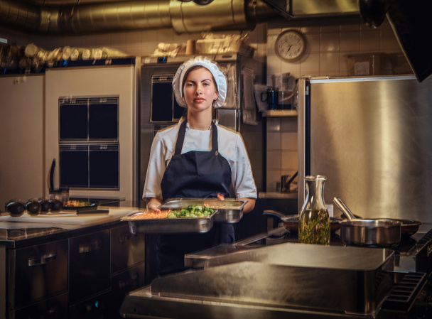 Restoranlar mutfak doğranmış sebze içeren bir kapsayıcı tutan bir üniforma giyen kadın şef. - Fotoğraf, Görsel