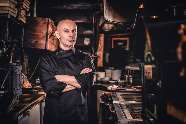 Confident chef posing with his arms crossed and looking at a camera in restaurant kitchen. - Foto, Bild