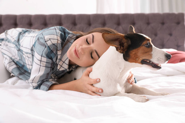 Beautiful woman with her dog lying in bed at home - Фото, изображение