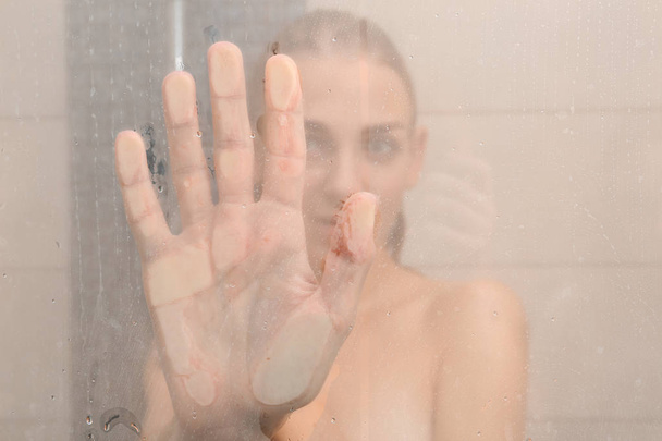 Jeune femme prenant une douche, vue par porte vitrée
 - Photo, image