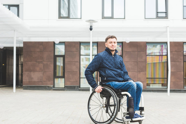 Young man in a wheelchair against the backdrop of a modern high-rise building. - Фото, зображення