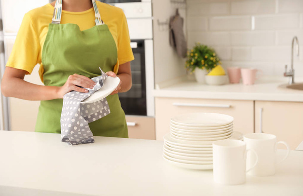 Young woman wiping clean plate in kitchen. Dish washing - Foto, afbeelding