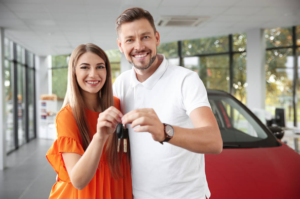 Happy man and woman with car keys in modern auto dealership - Фото, изображение