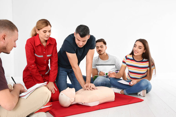 Group of people with instructor practicing CPR on mannequin at first aid class indoors - Fotó, kép