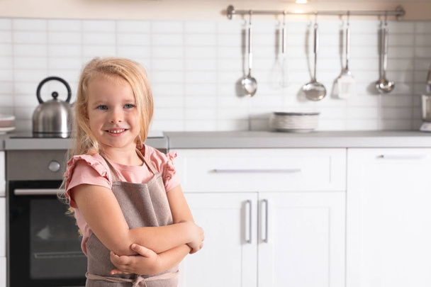 Cute little girl wearing apron near oven in kitchen. Space for text - Φωτογραφία, εικόνα