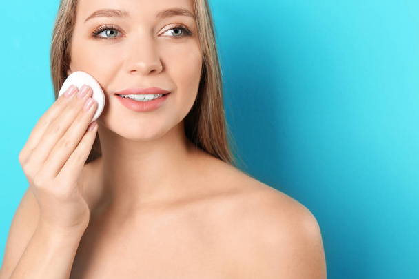 Portrait of beautiful young woman removing makeup with cotton pad on color background - Φωτογραφία, εικόνα