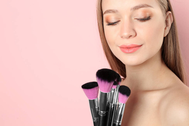 Portrait of beautiful young woman with makeup brushes on color background. Space for text - Foto, afbeelding