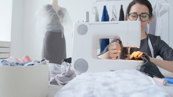 Concepto de pequeña empresa y hobby. Mujer joven diseñadora de ropa trabajando en una máquina de coser en su estudio
 - Metraje, vídeo