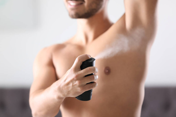 Handsome young man applying deodorant in room - Zdjęcie, obraz