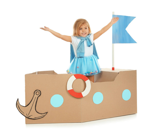 Cute little girl playing with cardboard ship on white background - Valokuva, kuva