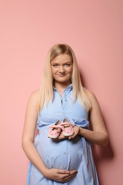 Beautiful pregnant woman in dress holding baby booties near tummy on color background - Fotografie, Obrázek