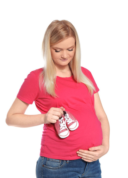 Beautiful pregnant woman holding baby booties near tummy on white background - Фото, зображення