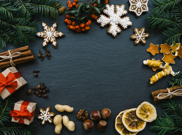 Frame with fir branches, cookies and Christmas decorations on dark stone background. Top view. - Fotoğraf, Görsel