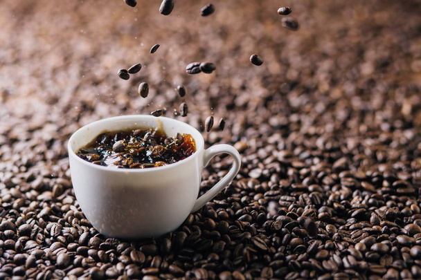 Coffee beans splashing into a mug filled with coffee on a background that completely consists of coffee beans - Photo, image