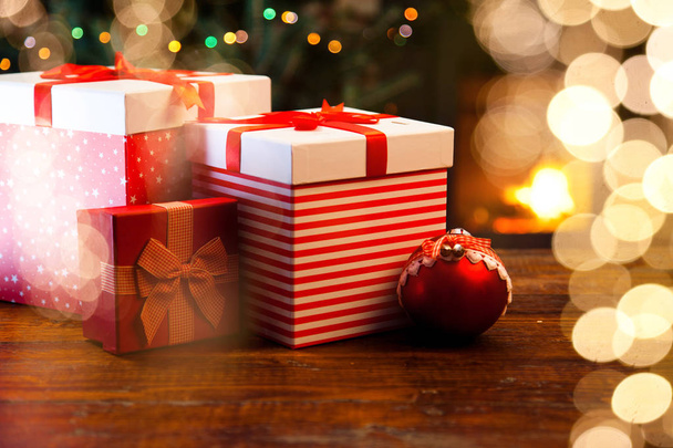 cajas de regalo rojas festivas de pie junto a la chimenea en llamas y el árbol de Navidad - acogedora casa
 - Foto, imagen