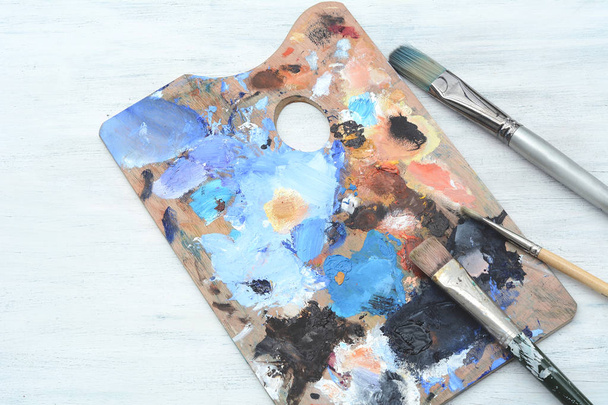 Artist's palette with colorful oil paint strokes and paintbrushes on wooden background. Art concept - Фото, зображення