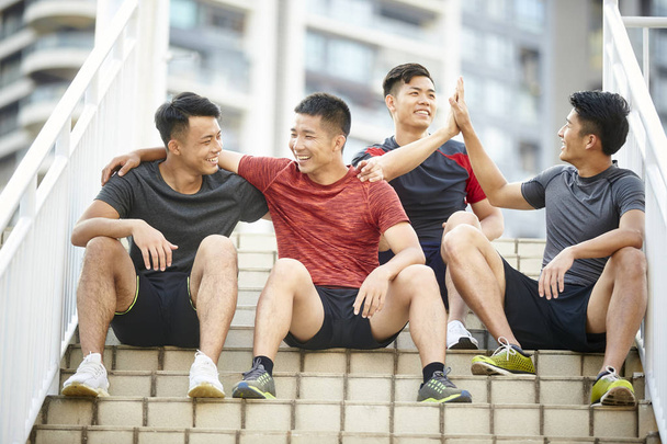 открытый портрет команды из четырех азиатских юных спортсменов, сидящих на ступеньках
 - Фото, изображение