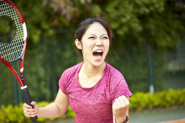 Aziatische meisje tennisspeelster vieren na een punt te hebben gescoord - Foto, afbeelding