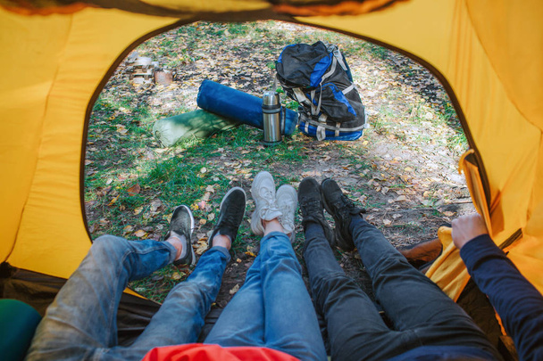 Three bodies lying in tent. Their feet are outside. They wear crosses. There is backpack with equipment outside. Man on right hold hand on tent. - Foto, Imagem