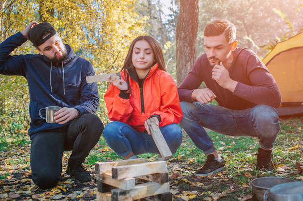 Three friends sitting in squad position and look at brickets of wood. Young woman hold one piece of it. They dont know what to do with it. People are frustrated. - Zdjęcie, obraz