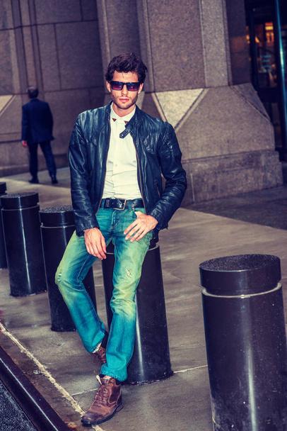 Man Casual Street Fashion. Dressing in black leather jacket, blue jeans, brown boot shoes, wearing sunglasses, a young European Businessman with beard sitting on street in New York, relaxing. - Photo, Image