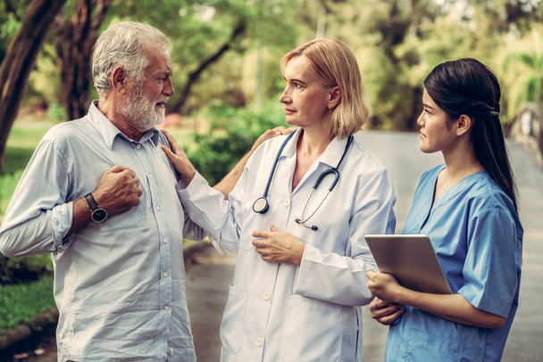 Senior man talking to doctor, nurse or caregiver in the park. Mature people healthcare and medical staff service concept. - Photo, Image
