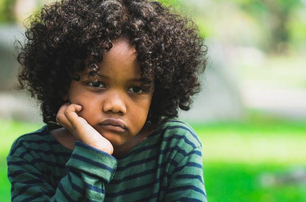 Un infeliz niño afroamericano aburrido sentado en el parque. El chico mostrando emociones negativas. Concepto de problemas infantiles
. - Foto, imagen