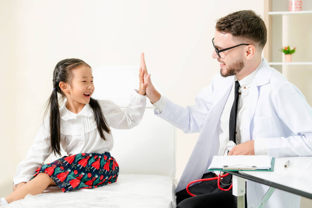 Young male doctor examining little kid in hospital office. The kid is happy and not afraid of the doctor. Medical children healthcare concept. - Photo, Image