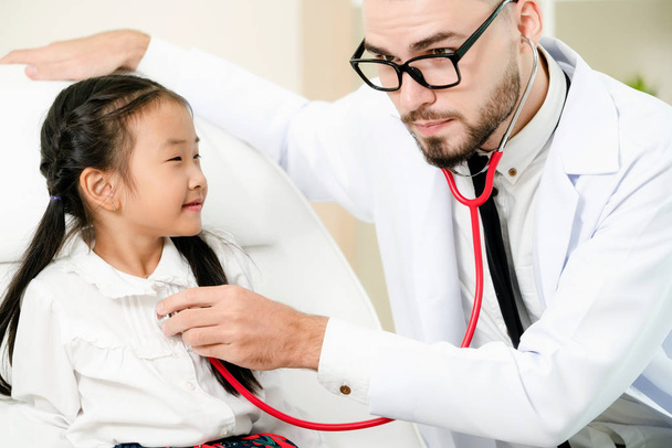 Young male doctor examining little kid in hospital office. The kid is happy and not afraid of the doctor. Medical children healthcare concept. - Foto, afbeelding