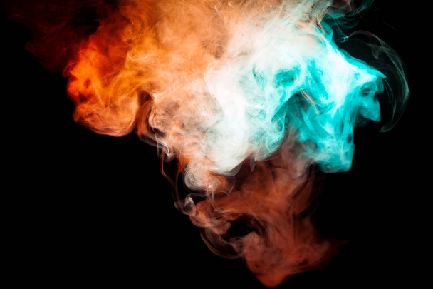 Φόντο πορτοκαλί, κόκκινες και πράσινες κυματιστές καπνού το σχήμα του κεφαλιού του φάντασμα ή ένας άνθρωπος με μυστικιστική εμφάνιση σε ένα μαύρο απομονωμένες έδαφος. Φωτεινό αφηρημένη φαντασία του ατμού από το vape. - Φωτογραφία, εικόνα