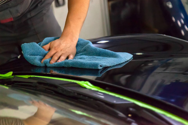 Close-up view on the hands of a male worker who rubs the hood of a car with a rag after polishing while working in a vehicle detectors workshop. - Photo, Image