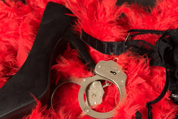 High heels, handcuffs and lingerie on a red feather pattern - Photo, Image