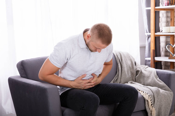 Young Man Sitting On Sofa Having Stomach Pain At Home - Photo, image