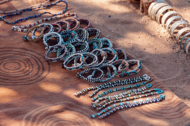 Himba halkından turistler için geleneksel hediyelik eşyalar kumlu topraklarda sergileniyor. Burası Afrika. Himba, Kuzey Namibya 'da, Kunene Bölgesi' nde yaşayan yerli halktır.) - Fotoğraf, Görsel