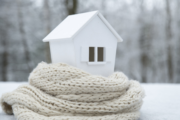 Haus im Winter - Heizungskonzept und kaltes, schneereiches Wetter mit Modell eines Hauses mit Strickmütze - Foto, Bild
