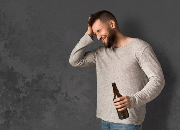 Junger Mann mit Kopfschmerzen hält Flasche Bier in der Hand - Foto, Bild