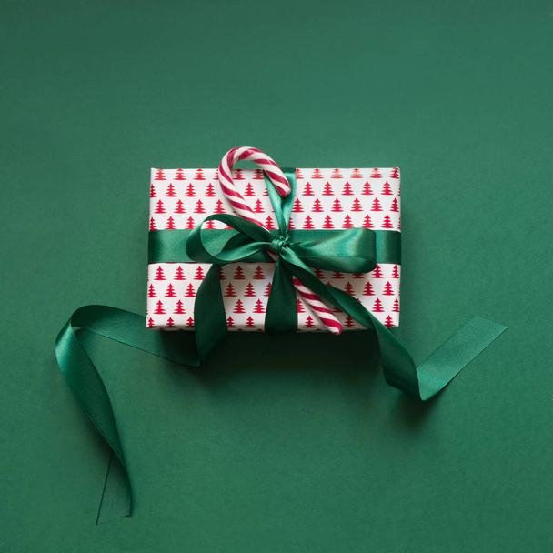 Christmas giftbox with candy cane on green surface. Xmas card. Top view. - Photo, image