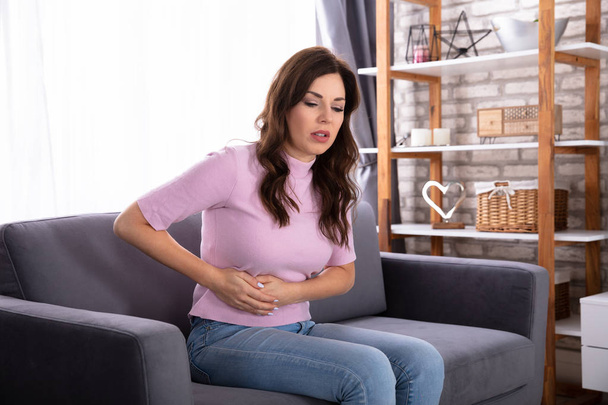 Young Woman Sitting On Sofa Suffering From Stomach Pain - Foto, immagini