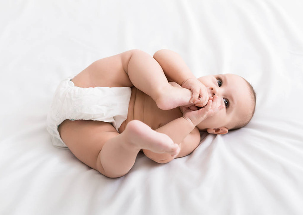 Adorable little baby sucking foot lying on bed - Fotó, kép