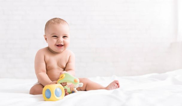 Bebê recém-nascido bonito brincando com brinquedos na cama
 - Foto, Imagem