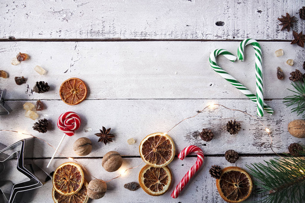 Christmas or New Year decoration, fir tree, tangerine, candy cane, dry oranges, sugar, walnuts and cookie cutters on white wooden background - Fotó, kép