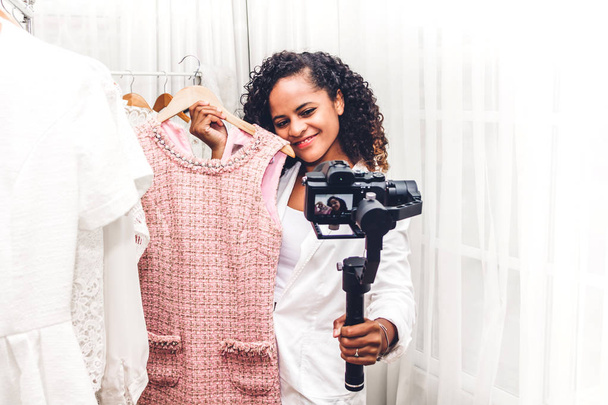 Blogger afroamericana parada frente a la cámara grabándose comprando y eligiendo ropa en una tienda.Compras de moda y concepto de redes sociales
 - Foto, imagen