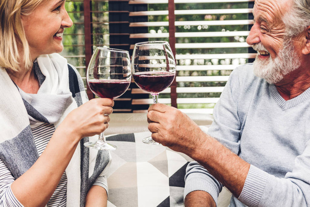 Couple sénior se détendre parler et boire des verres à vin ensemble sur le canapé dans le salon à la maison. - Photo, image