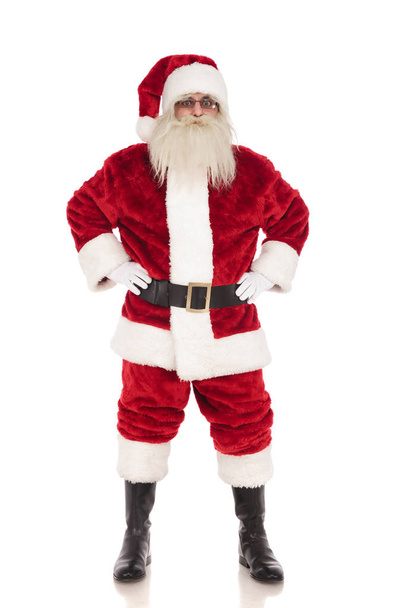 fröhlicher Weihnachtsmann steht auf weißem Hintergrund, während er seine Hüften hält, Ganzkörperbild - Foto, Bild