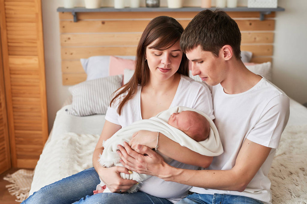 junge Eltern mit einem Neugeborenen zu Hause auf dem Bett - Foto, Bild