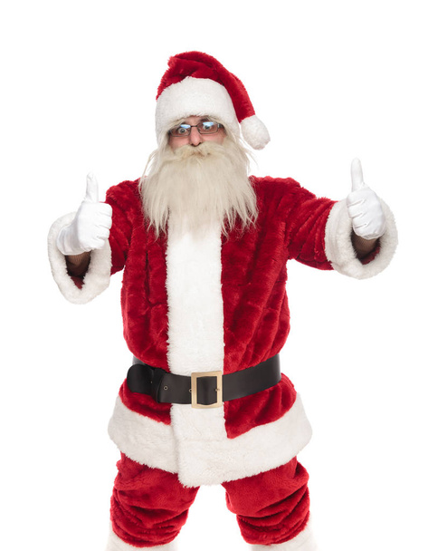 портрет Санта-Клауса в очках, делая большие пальцы вверх знак, стоя на белом фоне
 - Фото, изображение