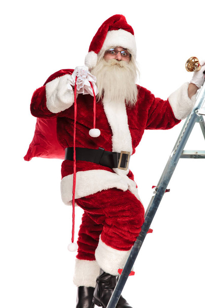 Santa lép fel a létrán, hogy ajándékokat karácsonyra állva, fehér háttér, teljes hosszúságú kép - Fotó, kép