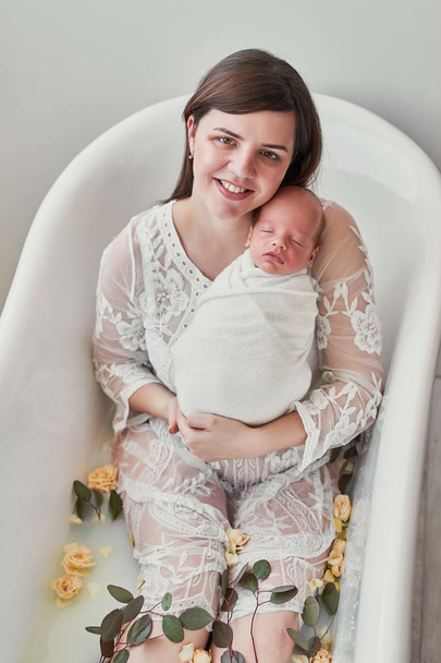 νεαρή μητέρα με ένα νεογέννητο μωρό σε ένα λουτρό γάλακτος με λουλούδια - Φωτογραφία, εικόνα