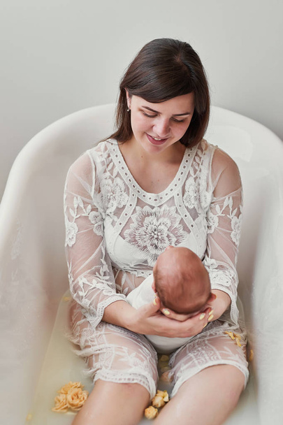 fiatal anya egy újszülött baba tejet fürdőbe, virágok - Fotó, kép