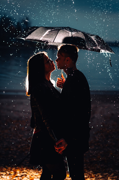 young man and woman under an umbrella and rain. - Фото, зображення